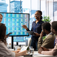 Team working in an office, looking at an electronic stock market board.