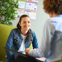 Woman in a clinic speaking with a clinician sitting by a notice board.