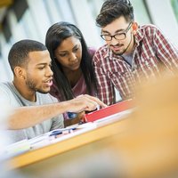 Three people sat down looking at some documents on a desk.