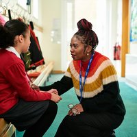 Image of female teacher attentively listening to child sat on a bench.