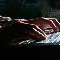 Image of hands typing on a keyboard in a dark room.