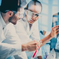 Image of two scientists wearing safety glasses discussing a chart on a screen.
